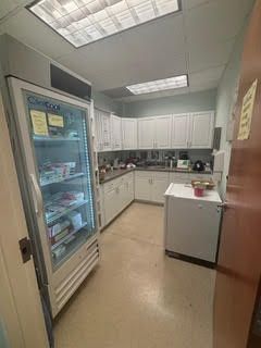 A commercial kitchen with a tall refrigerator, white cabinets, and a prep area.
