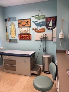 Doctor's office exam room with nautical decor on the wall, including a surfboard and whale signs.