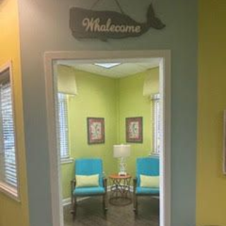 A doorway with a whale-shaped sign above leads to a brightly colored waiting room with blue chairs.