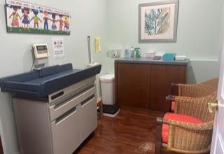 Examination room with a changing table, cabinet, chairs, and artwork.