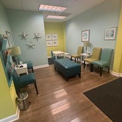 Waiting room with chairs, ottoman, small tables, and artwork on the wall.