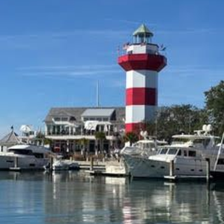 Red and white striped lighthouse at a harbor, boats docked, blue sky.