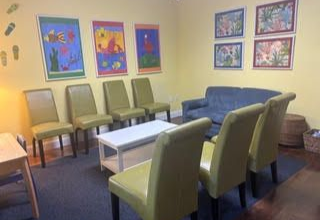 Waiting room with yellow walls, colorful art, chairs, a couch, and a small table.