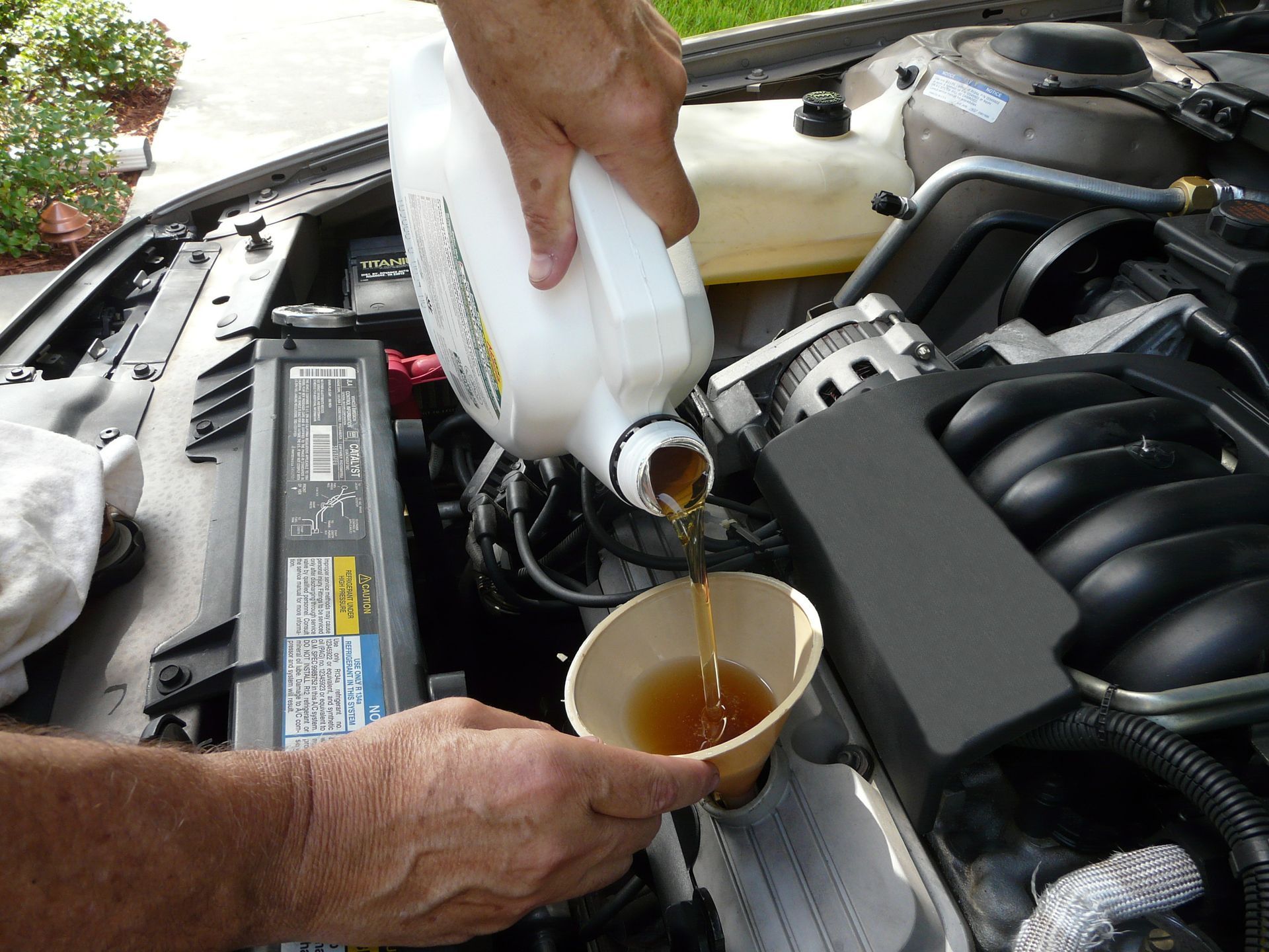 A person is pouring oil into a cup under the hood of a car