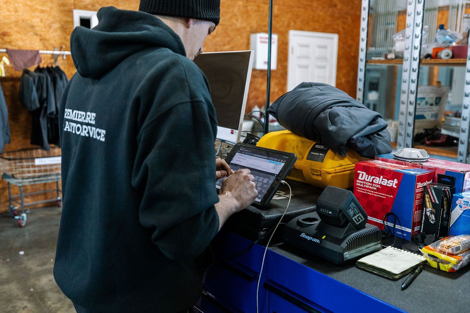 A man in a black hoodie is using a laptop computer in a garage.