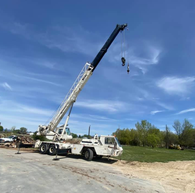 White crane truck on a paved lot with its boom extended against a blue sky.