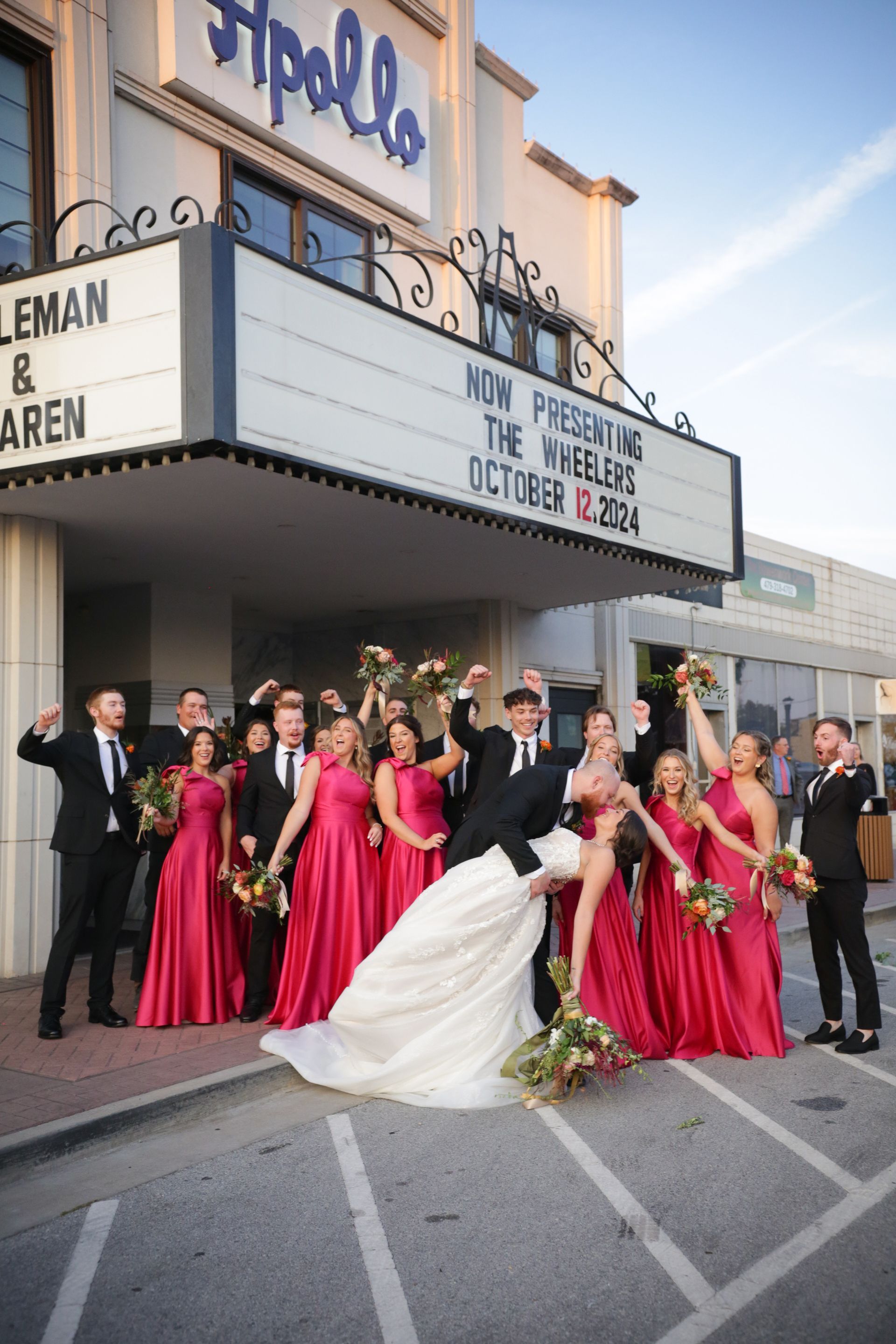 Wedding party posing in front of the Apollo Theater. Bride dipped backward, surrounded by bridesmaids in pink dresses.
