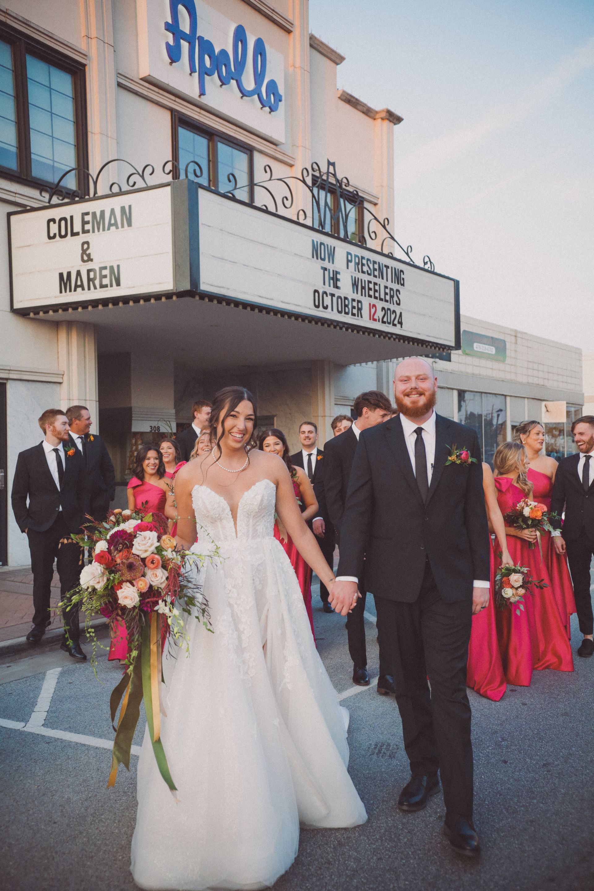 Bride and groom walk hand-in-hand in front of the Apollo Theater with wedding party following.