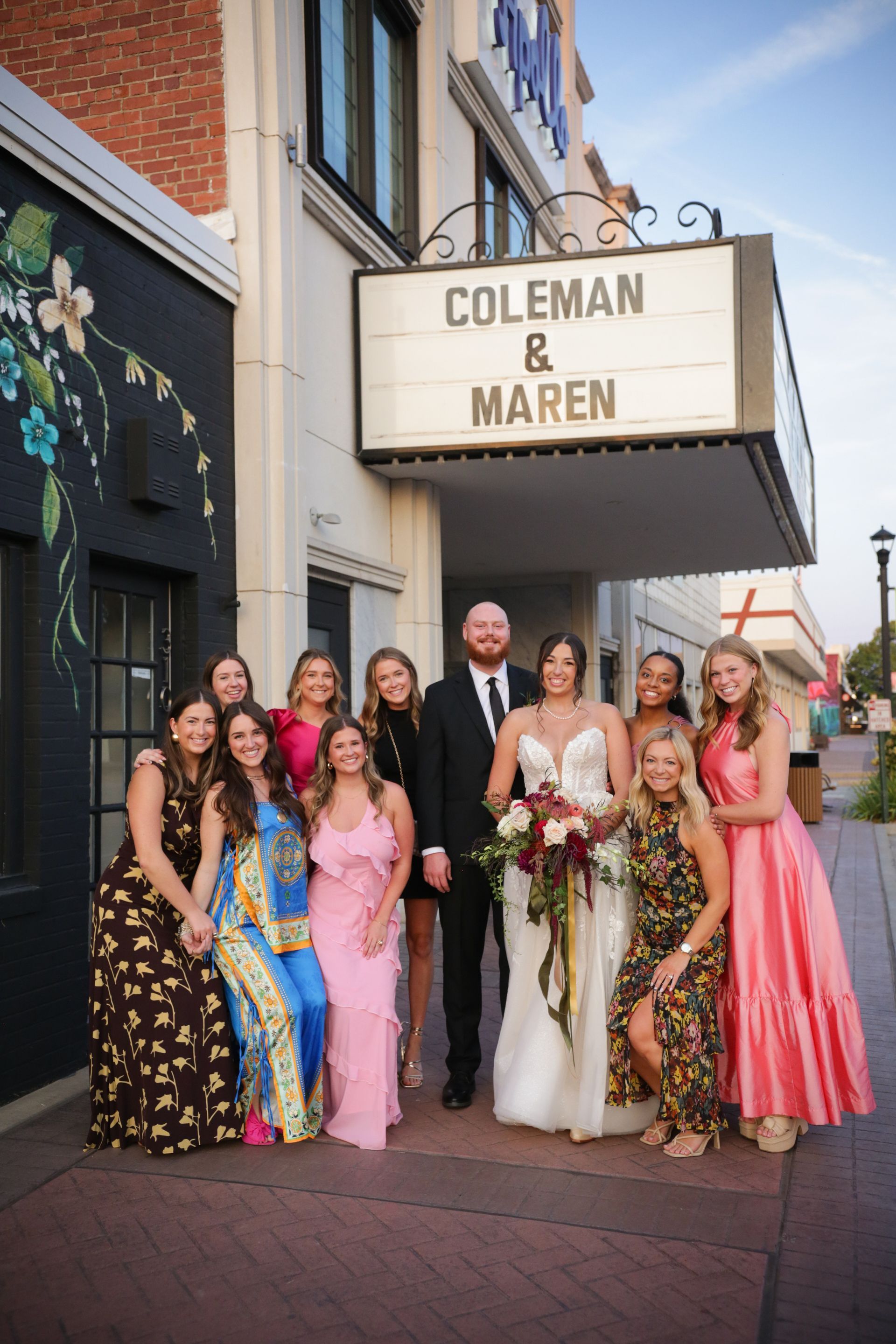 Wedding group poses under marquee that reads 