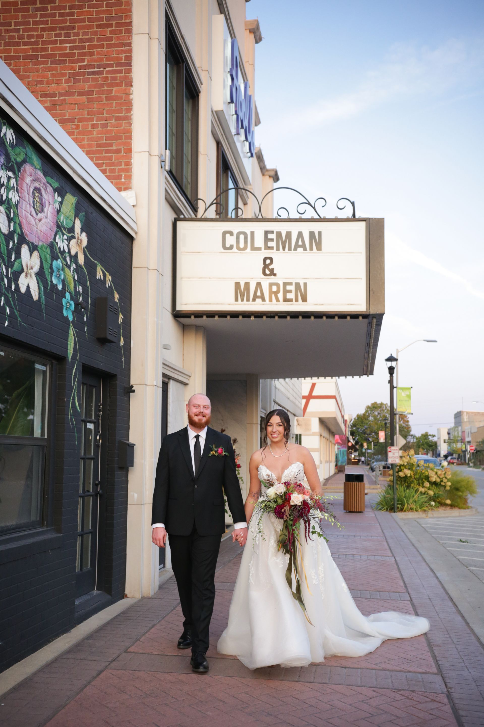 Bride and groom walk hand-in-hand in front of a theater marquee that reads 