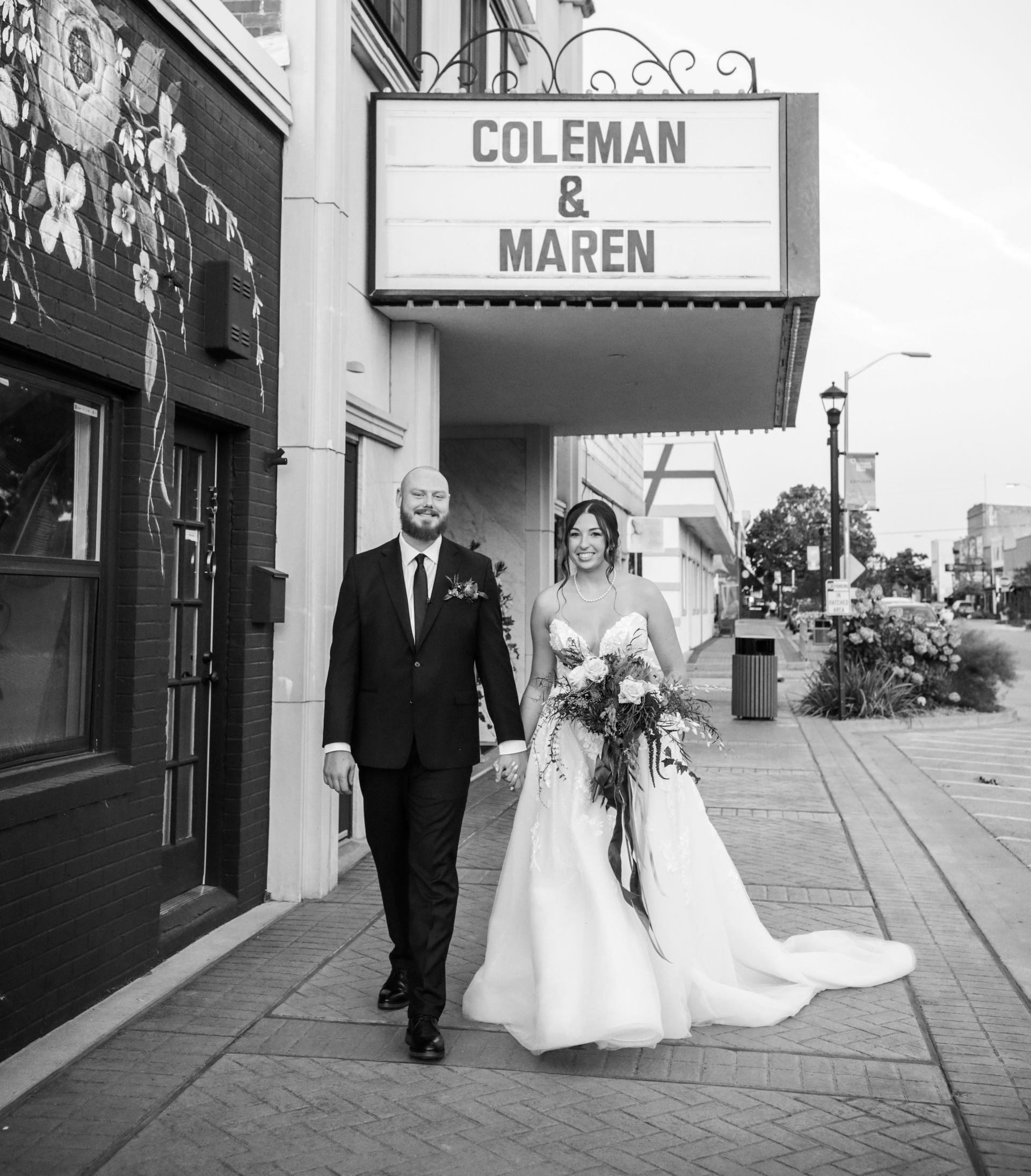 Bride and groom walk hand-in-hand down a sidewalk in front of a theater marquee. Sign reads: Coleman & Maren.
