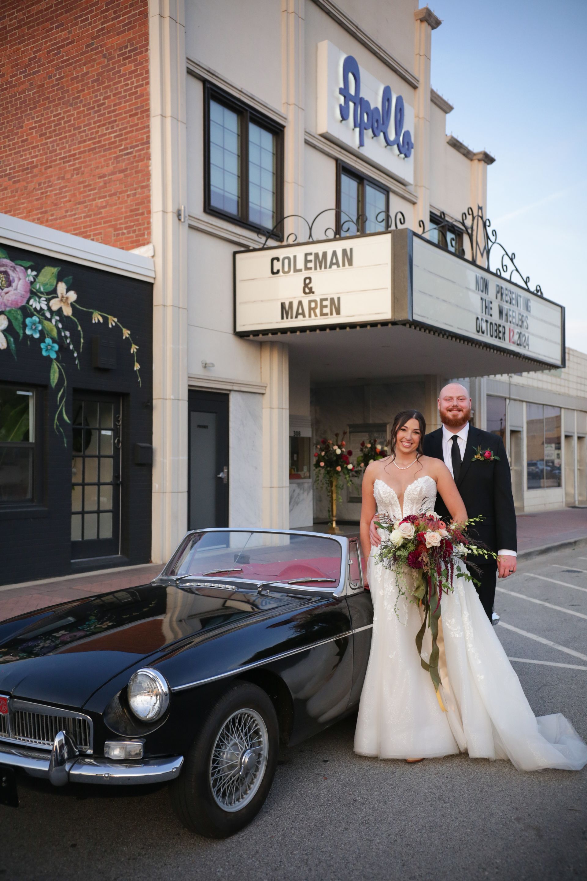 Bride and groom pose by black convertible in front of Apollo Theater. Sign reads 