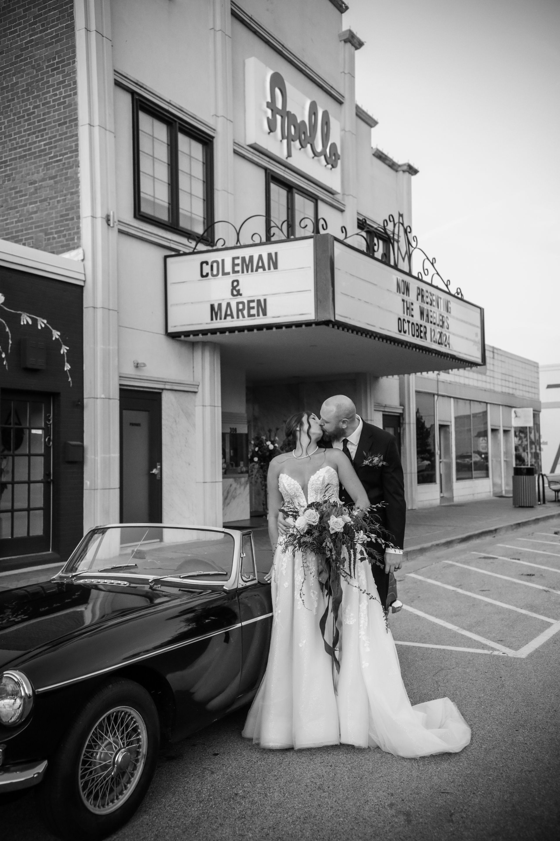 Wedding couple kissing in front of the Apollo Theater, beside a classic black car.