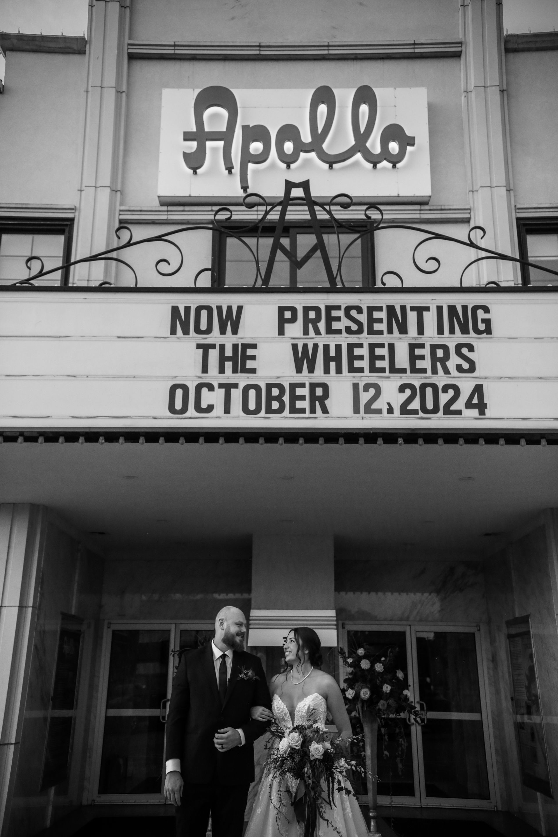Bride and groom pose in front of the Apollo Theater, the marquee announces 