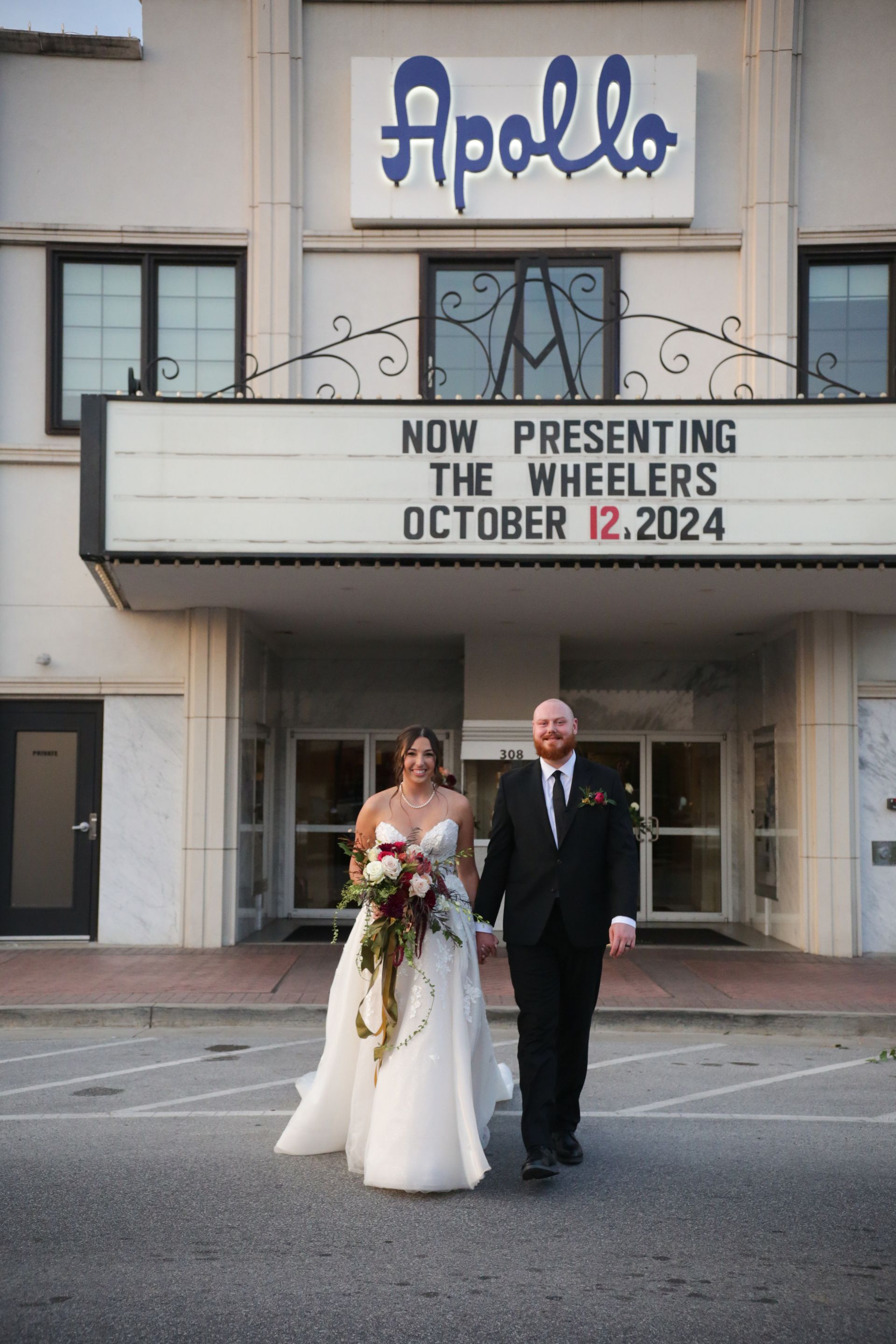 Bride and groom walk hand-in-hand in front of the Apollo Theater. Marquee says 