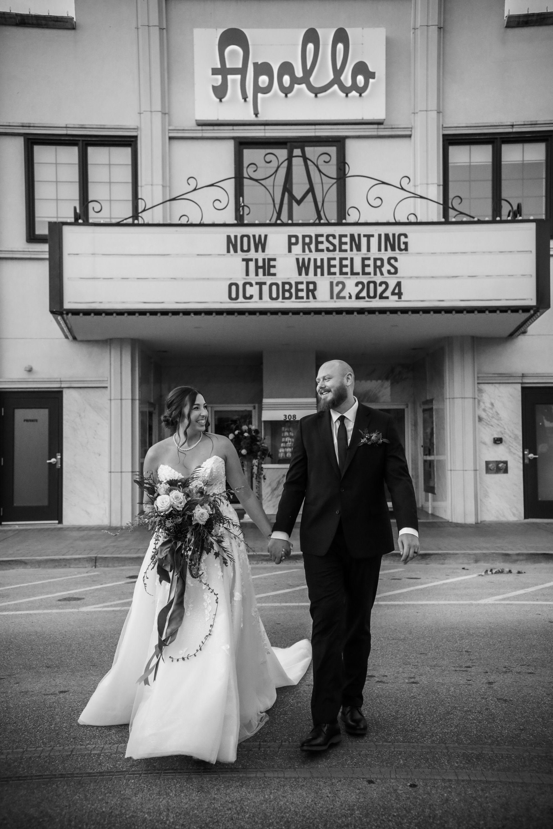 Bride and groom holding hands, smiling, walking in front of the Apollo Theater marquee announcing 