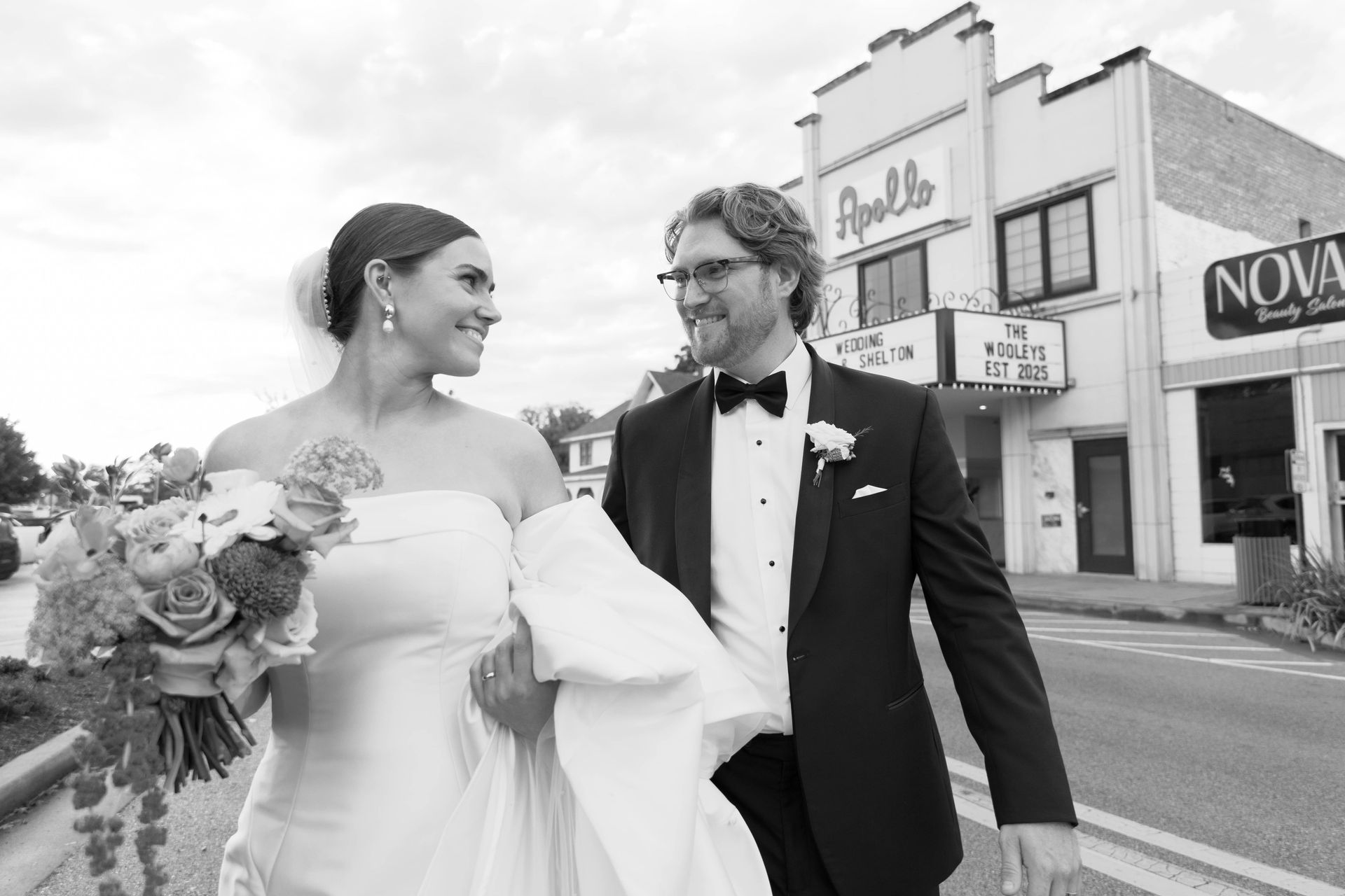 Bride and groom walking, looking at each other, near a theater. Black and white.