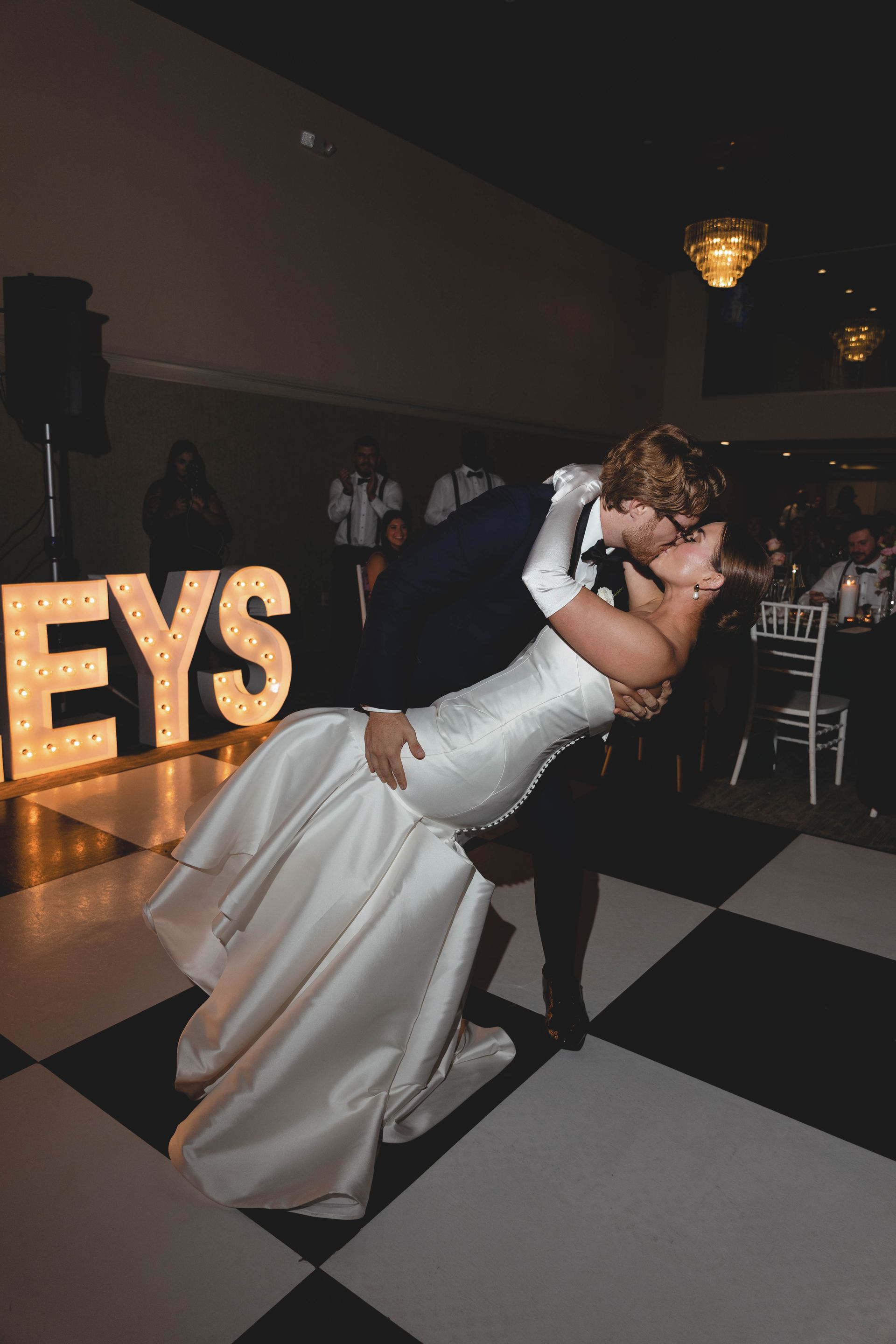 Crowd at a nightclub with DJ Bryan, raised hands, colorful lights, and a stage.