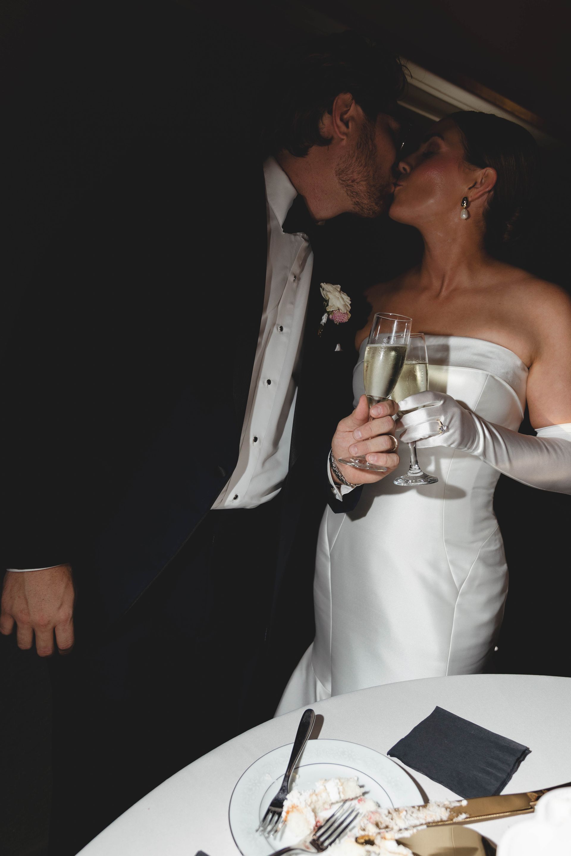 Bride and groom kissing, holding champagne flutes, wedding reception.
