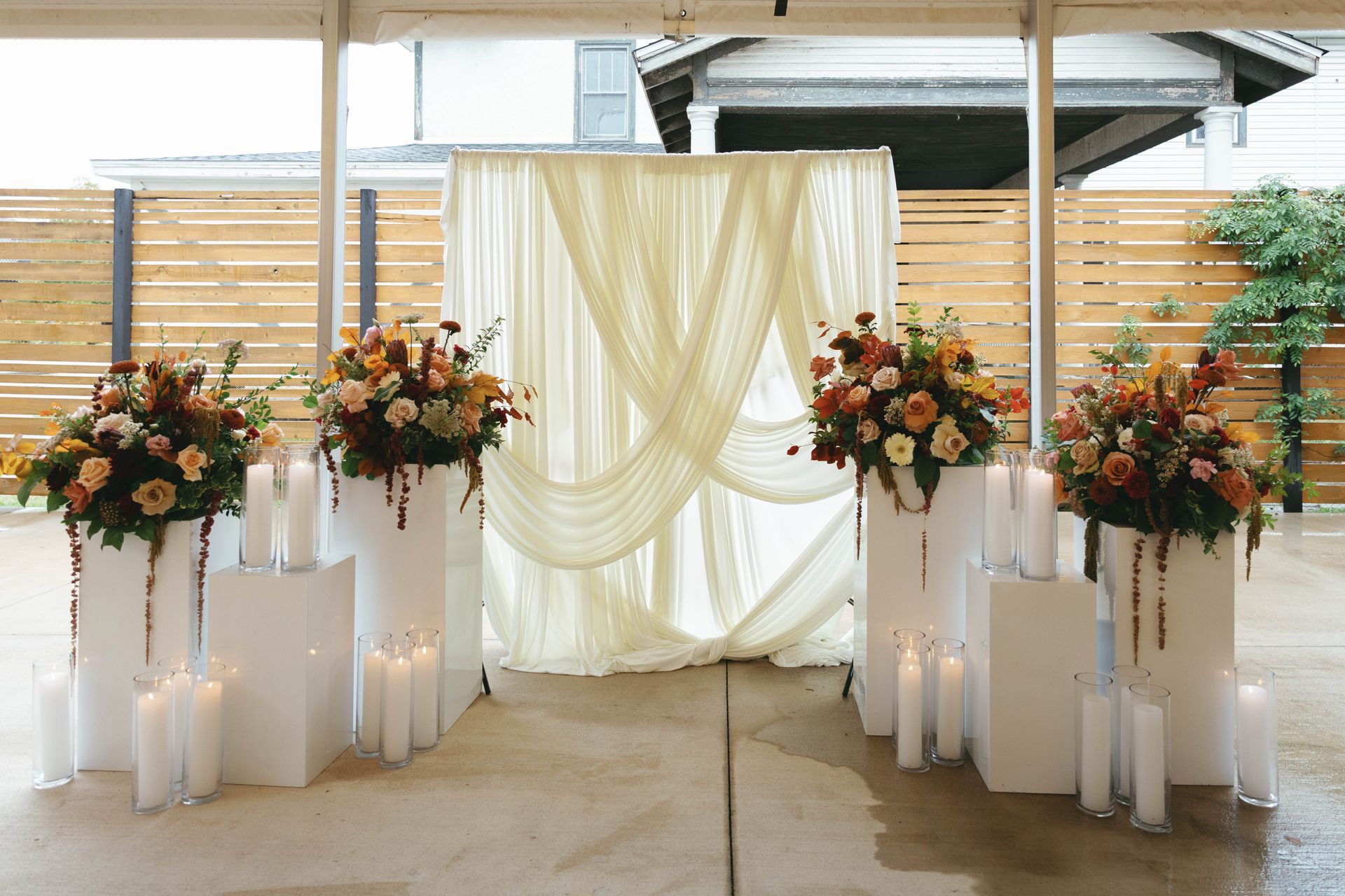 Wedding altar with floral arrangements, candles, and draped fabric backdrop.