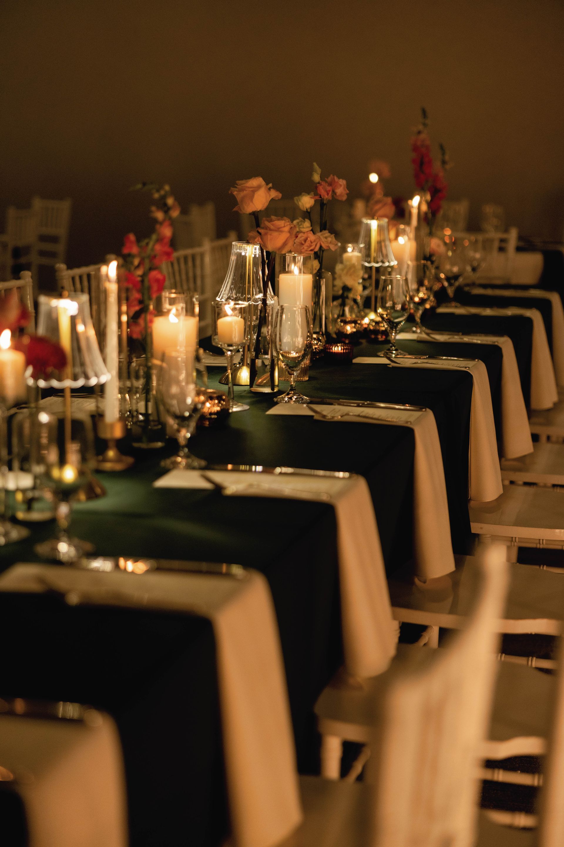 Long table set for a formal event, featuring green tablecloths, white accents, and candlelight.