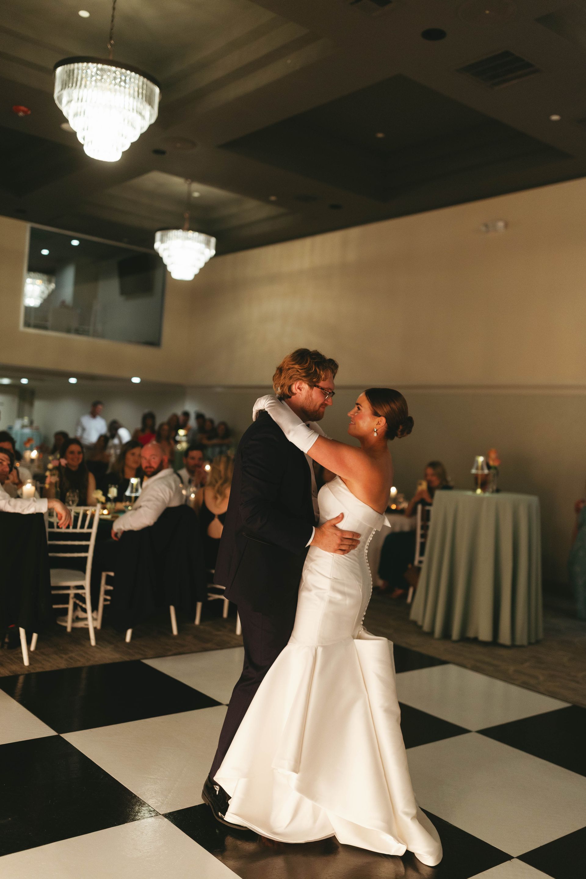 Bride and groom dance on a black and white checkered floor at a wedding reception.