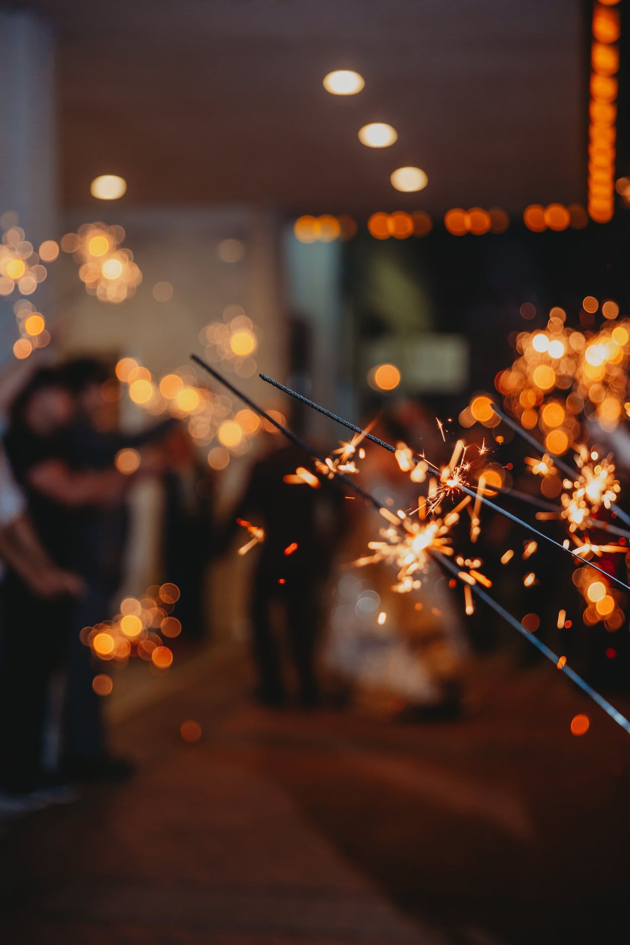 Sparklers illuminate a wedding exit. People in silhouette. Warm, blurred background.