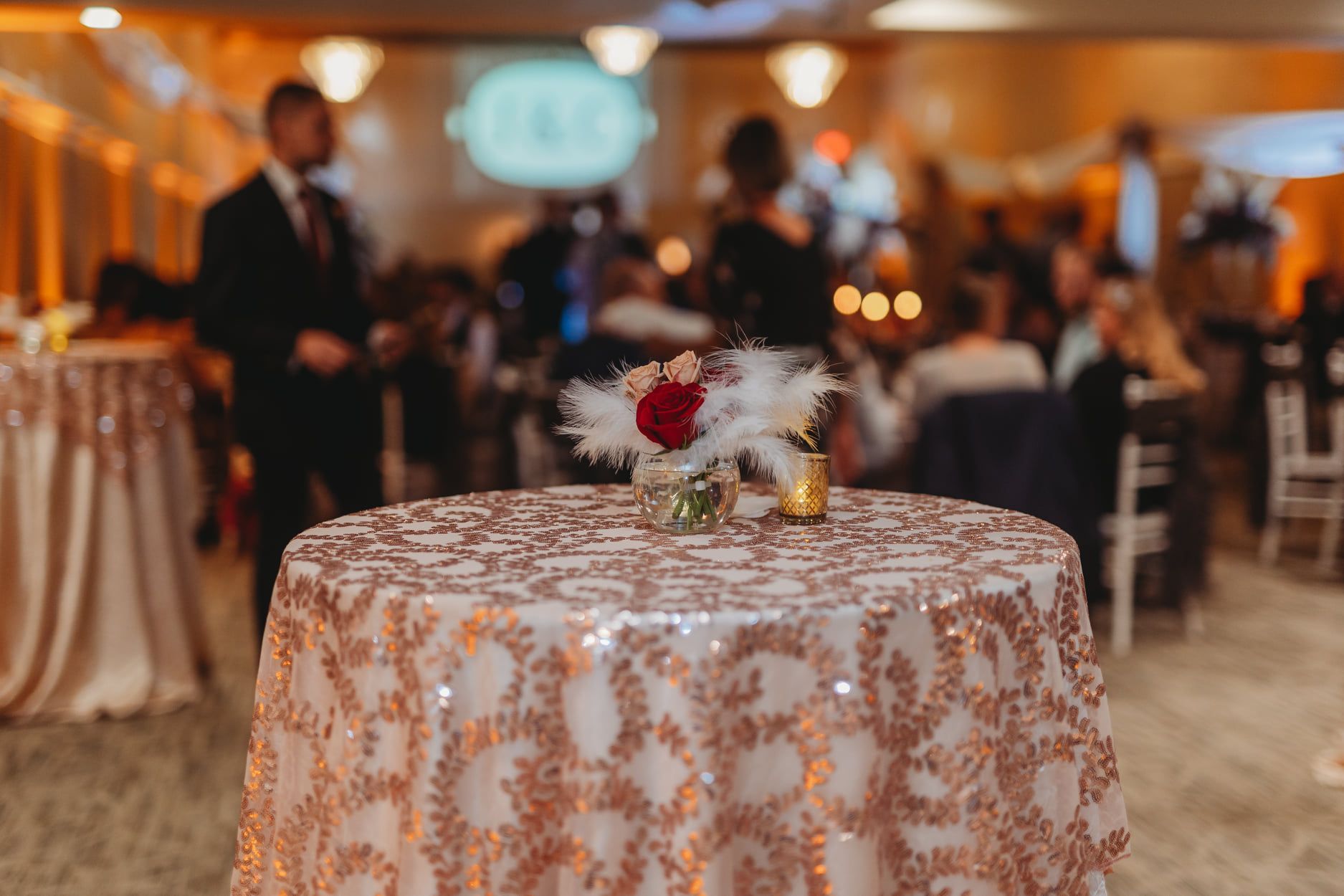 Round table with a rose-gold sequin tablecloth, flower arrangement, and blurred event background.
