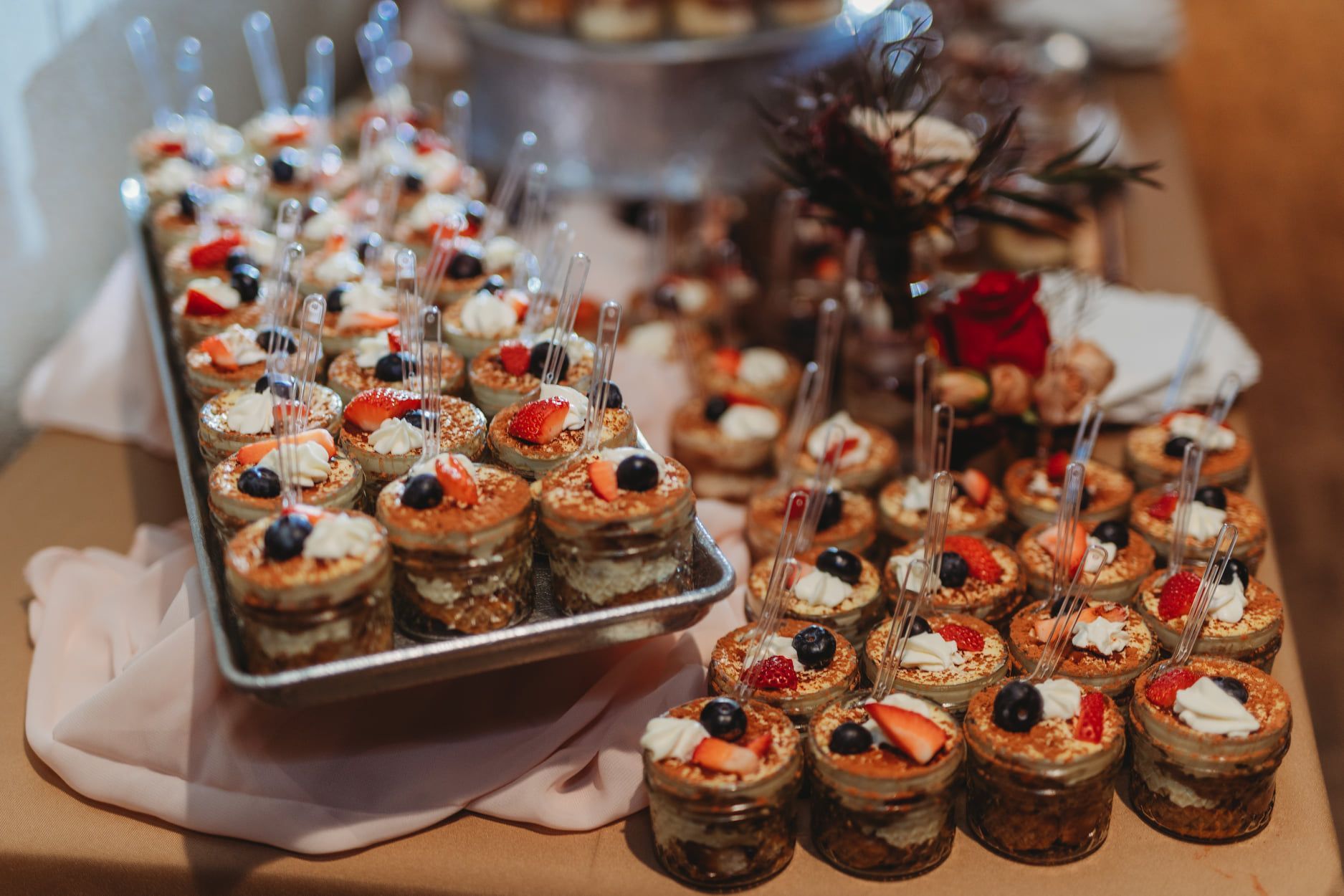 Dessert jars with cream, berries, and crumbs on a tray, arranged for a party.