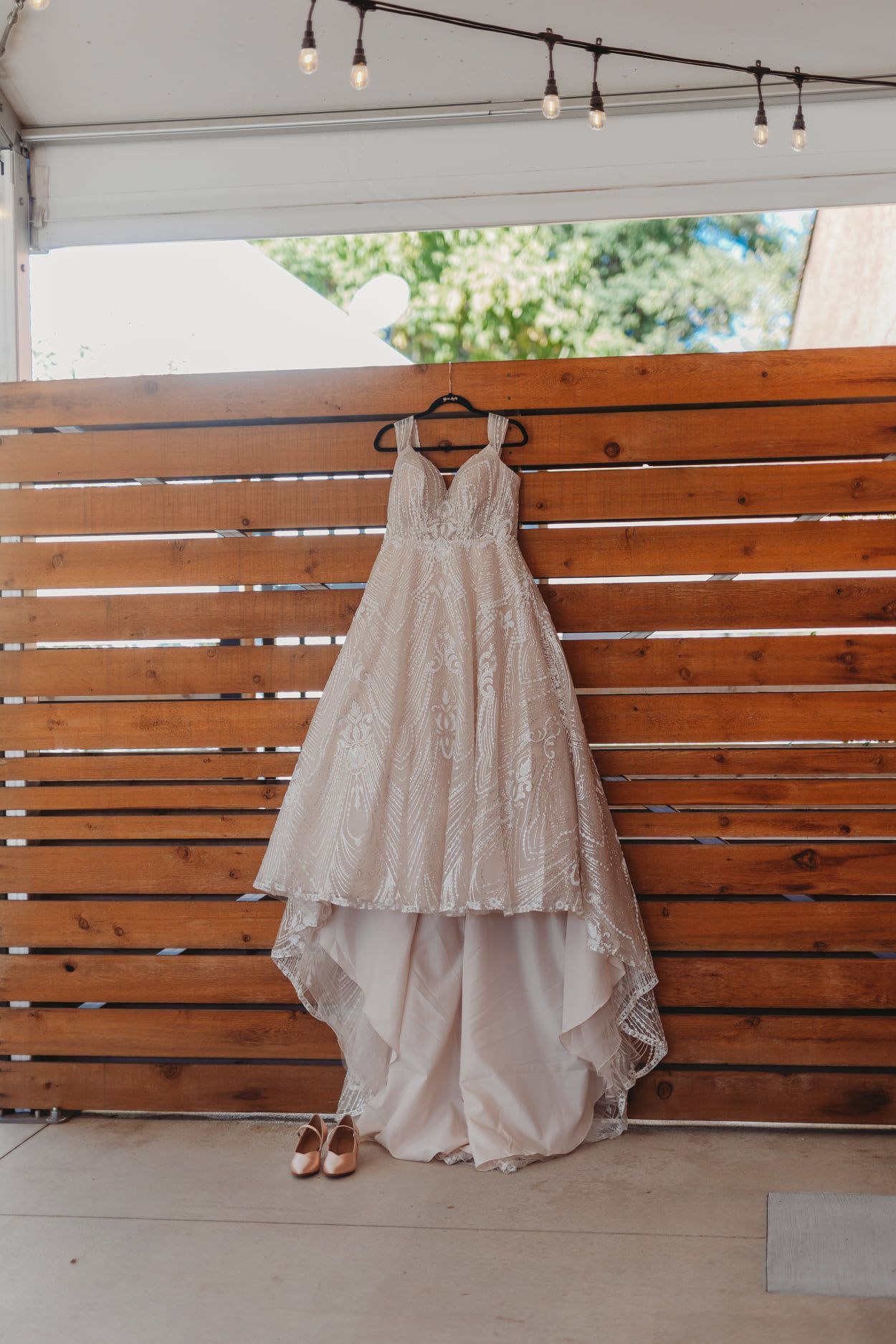 Wedding dress hanging on a wooden wall, with shoes below.