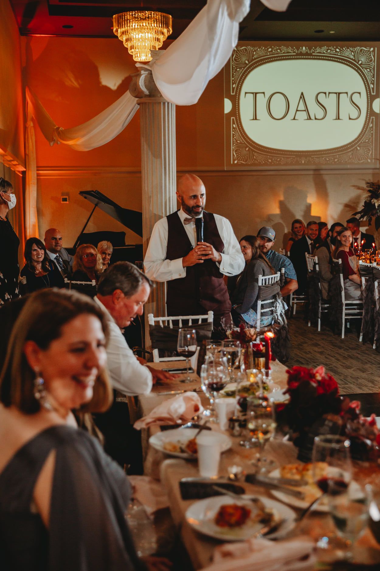 Man giving a toast at a wedding reception. Guests at tables, 