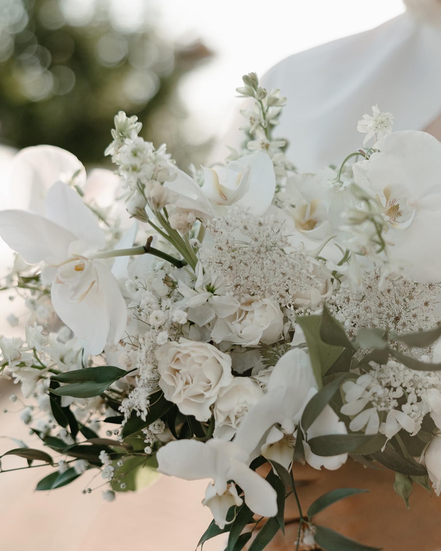 Close-up of an all-white floral arrangement with orchids, roses, and greenery.