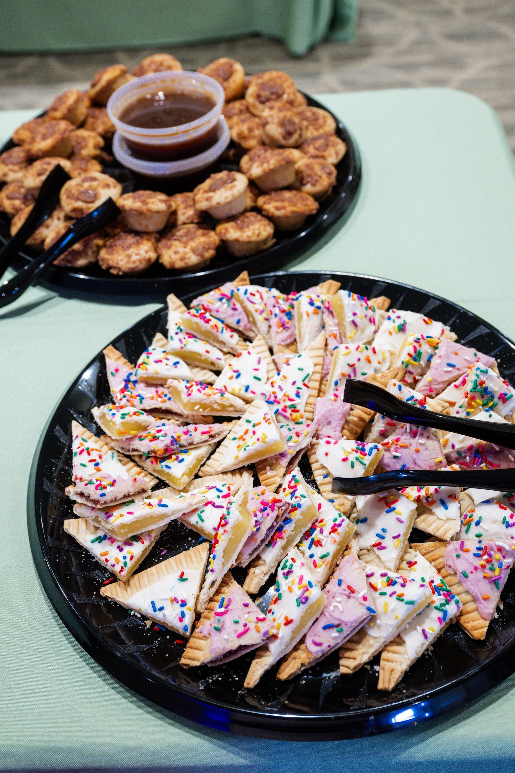 Two platters of pastries: cinnamon bites with dip, and triangle-shaped frosted cookies with sprinkles.