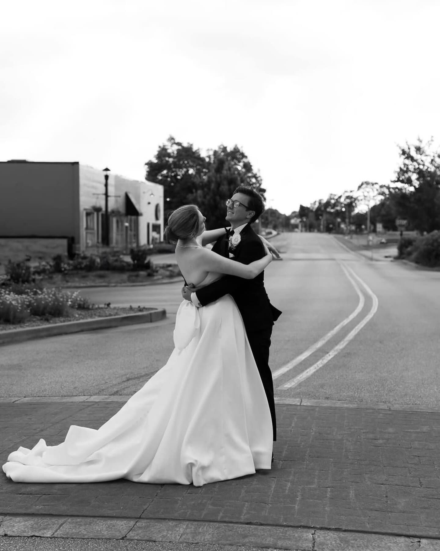 Bride and groom embrace in a street, black and white. Bride wears a strapless gown; groom in a tuxedo.
