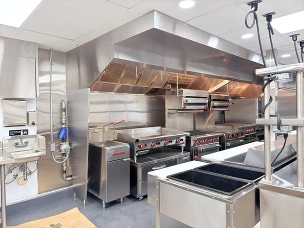 Commercial kitchen with stainless steel appliances and ventilation hood.