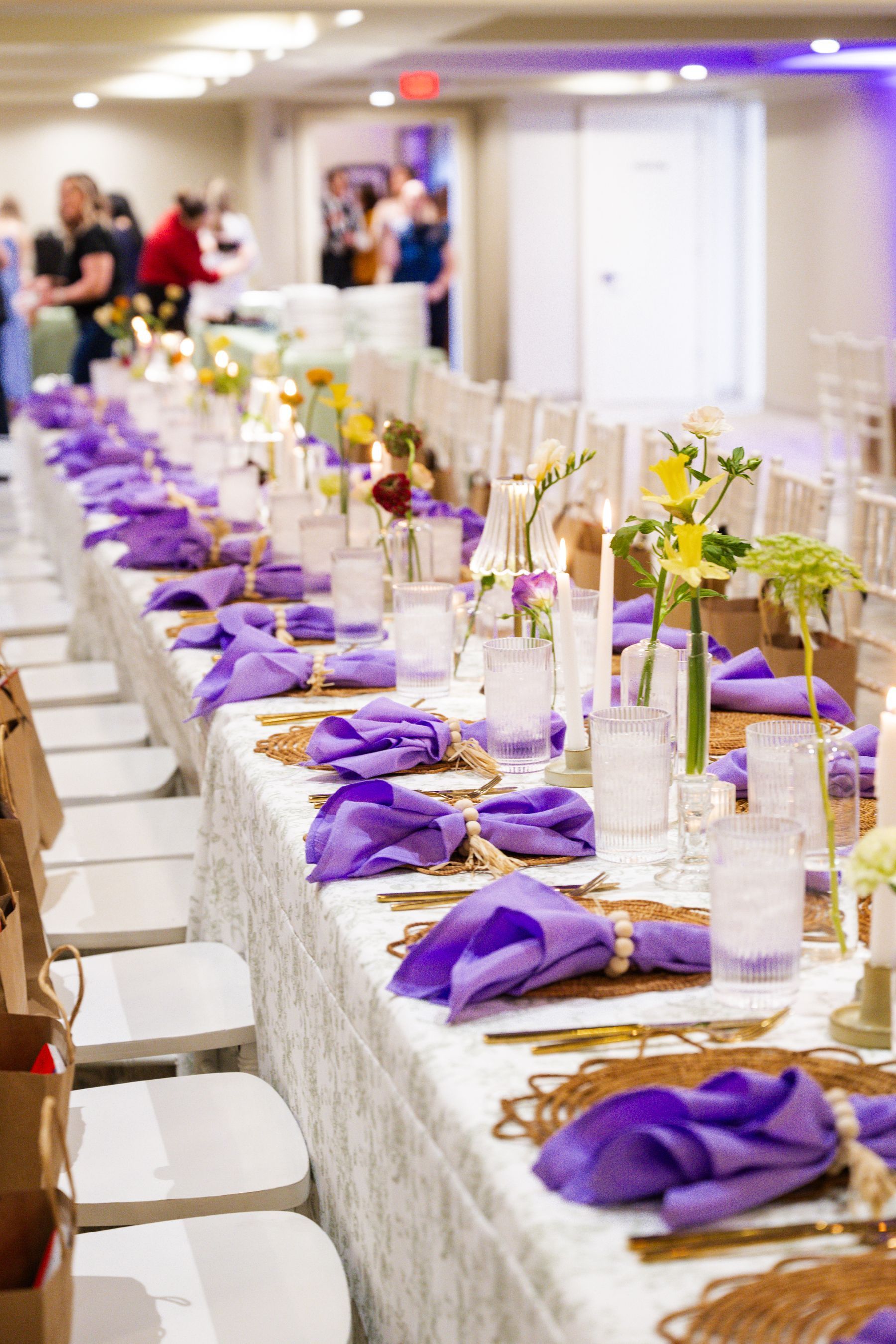 Long table set for an event with purple napkins and floral centerpieces.