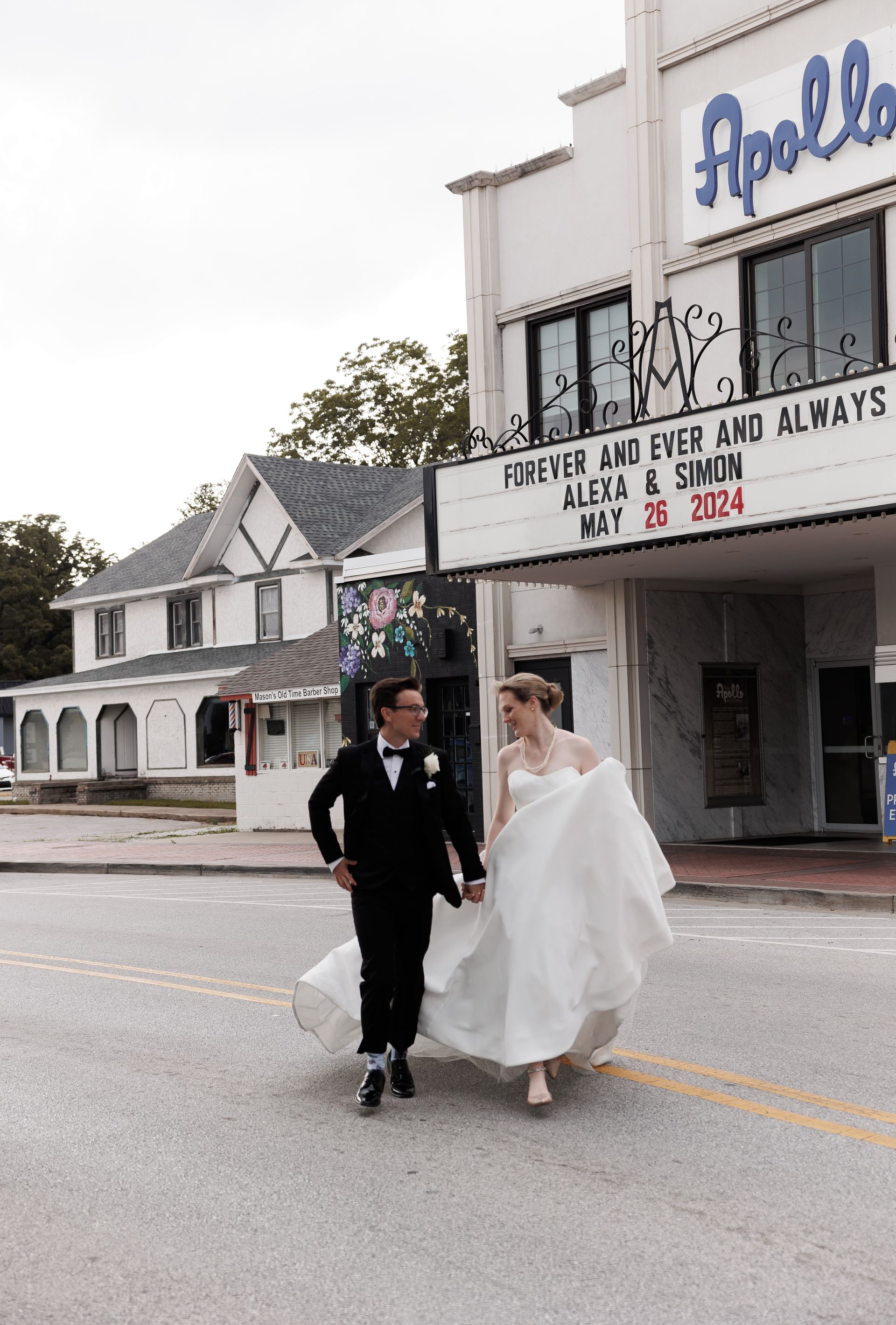 Newlyweds walk hand-in-hand across a street in front of the Apollo Theater.