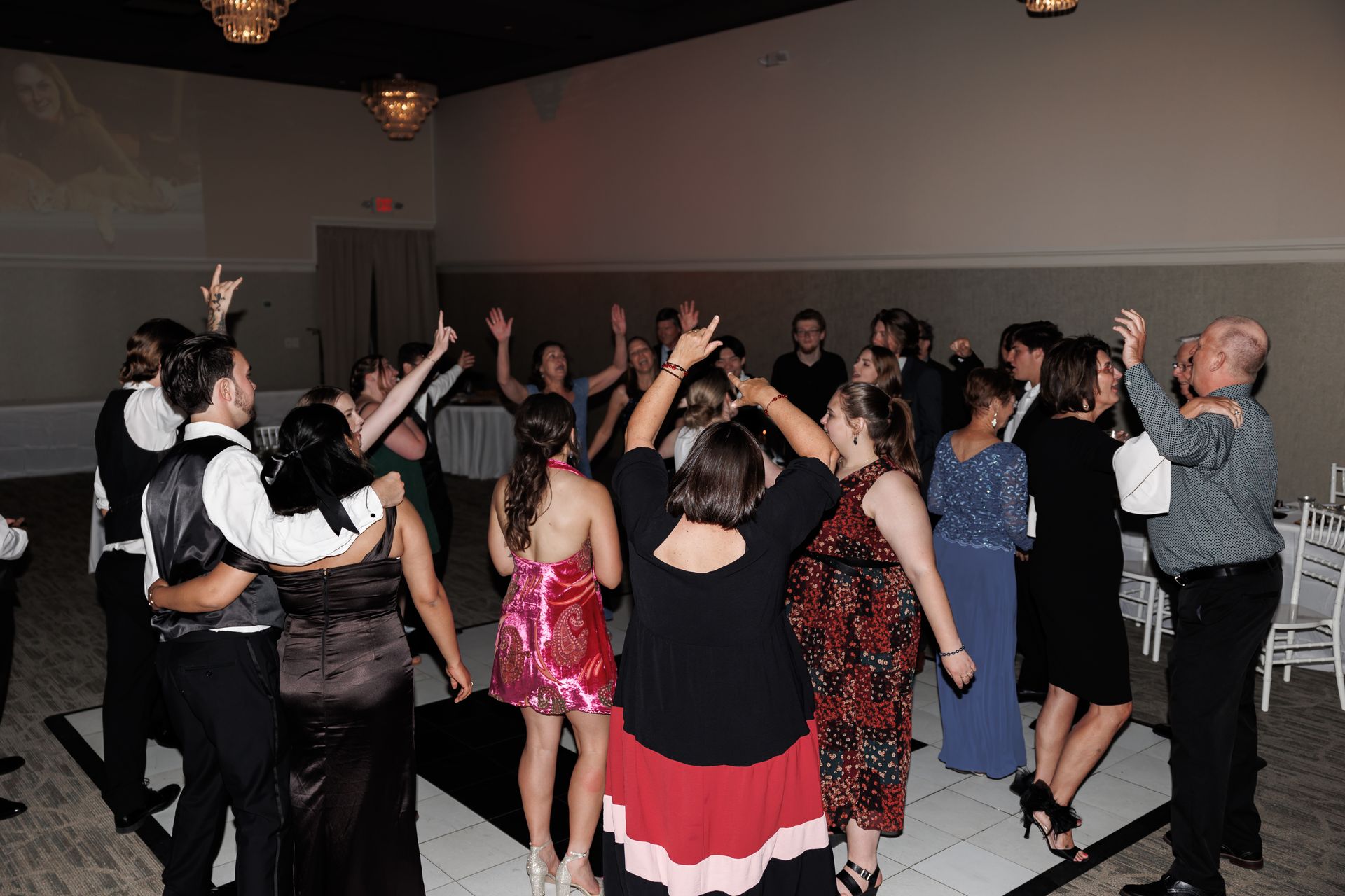 People dancing on a checkered dance floor in a well-lit room. Arms raised, celebrating.