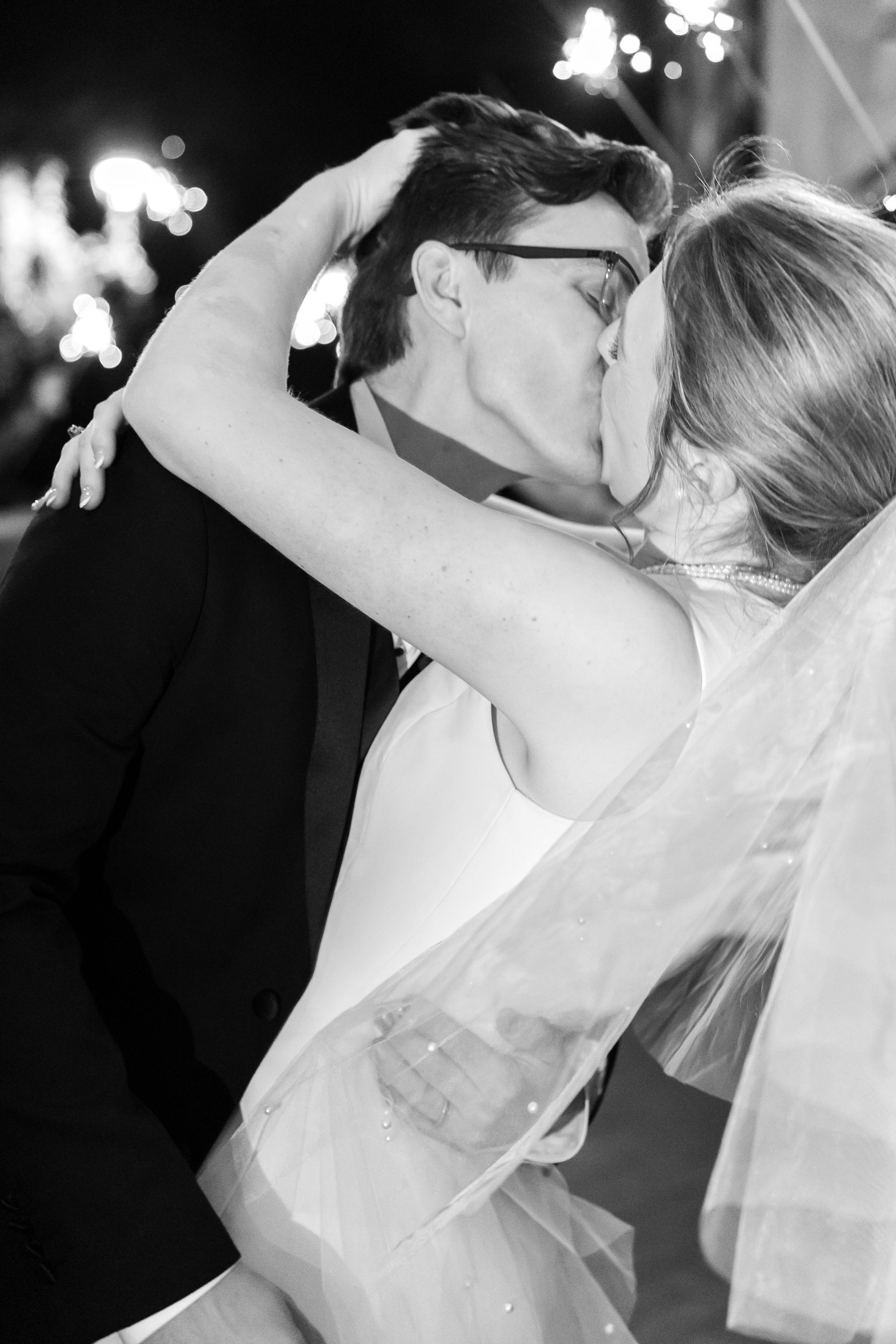 Couple kissing, groom in suit, bride in veil, outside.