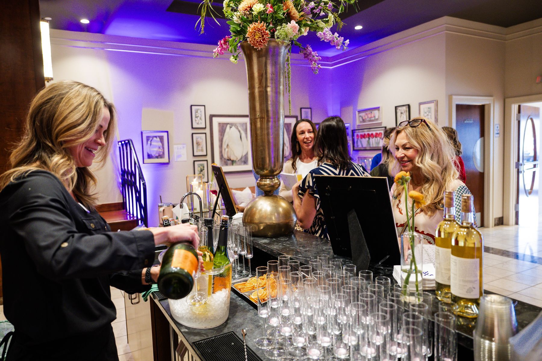 Bartender pouring champagne at an event; guests laughing at the bar.