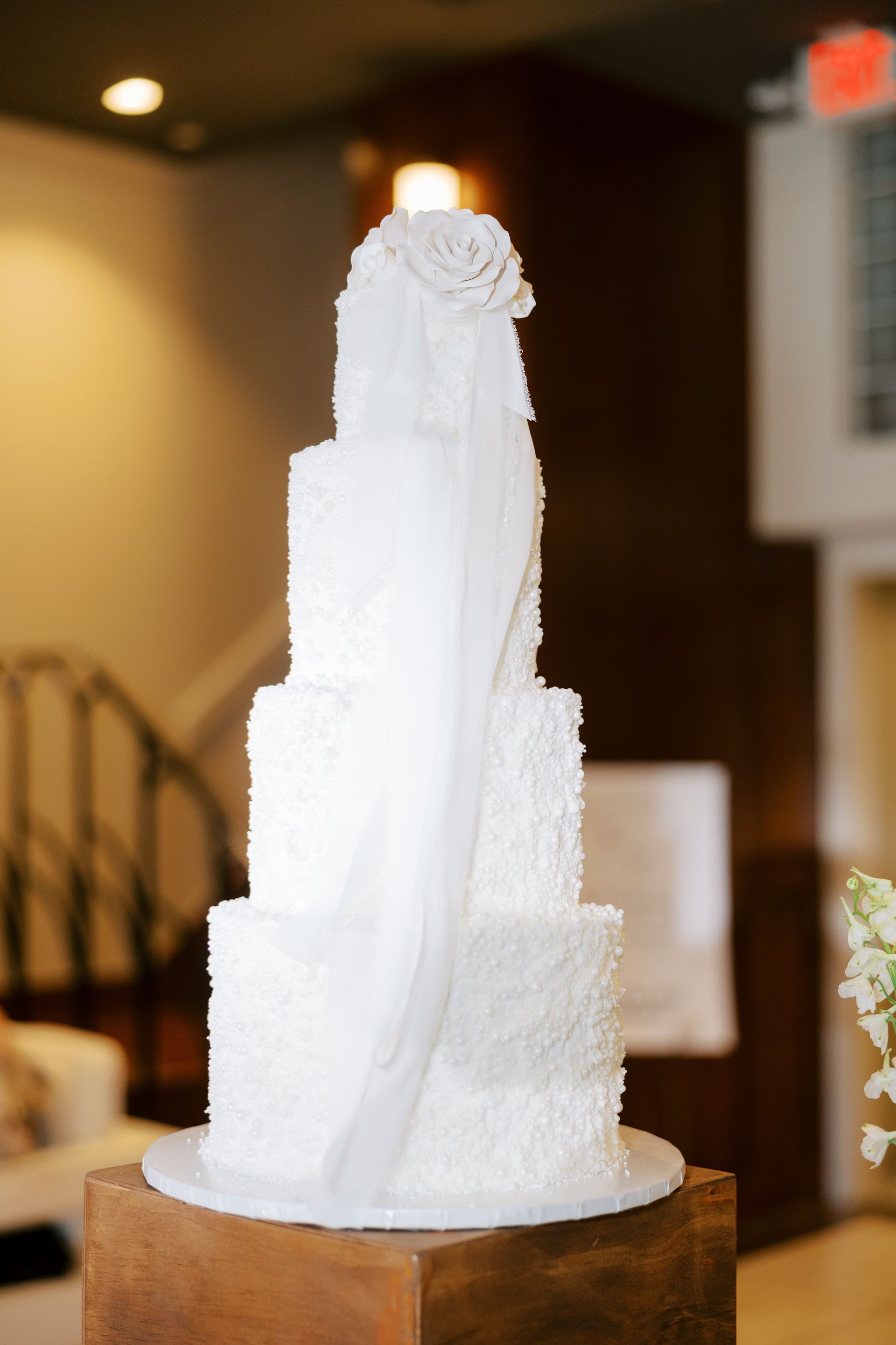 White wedding cake with textured frosting and a veil, on a wooden stand.