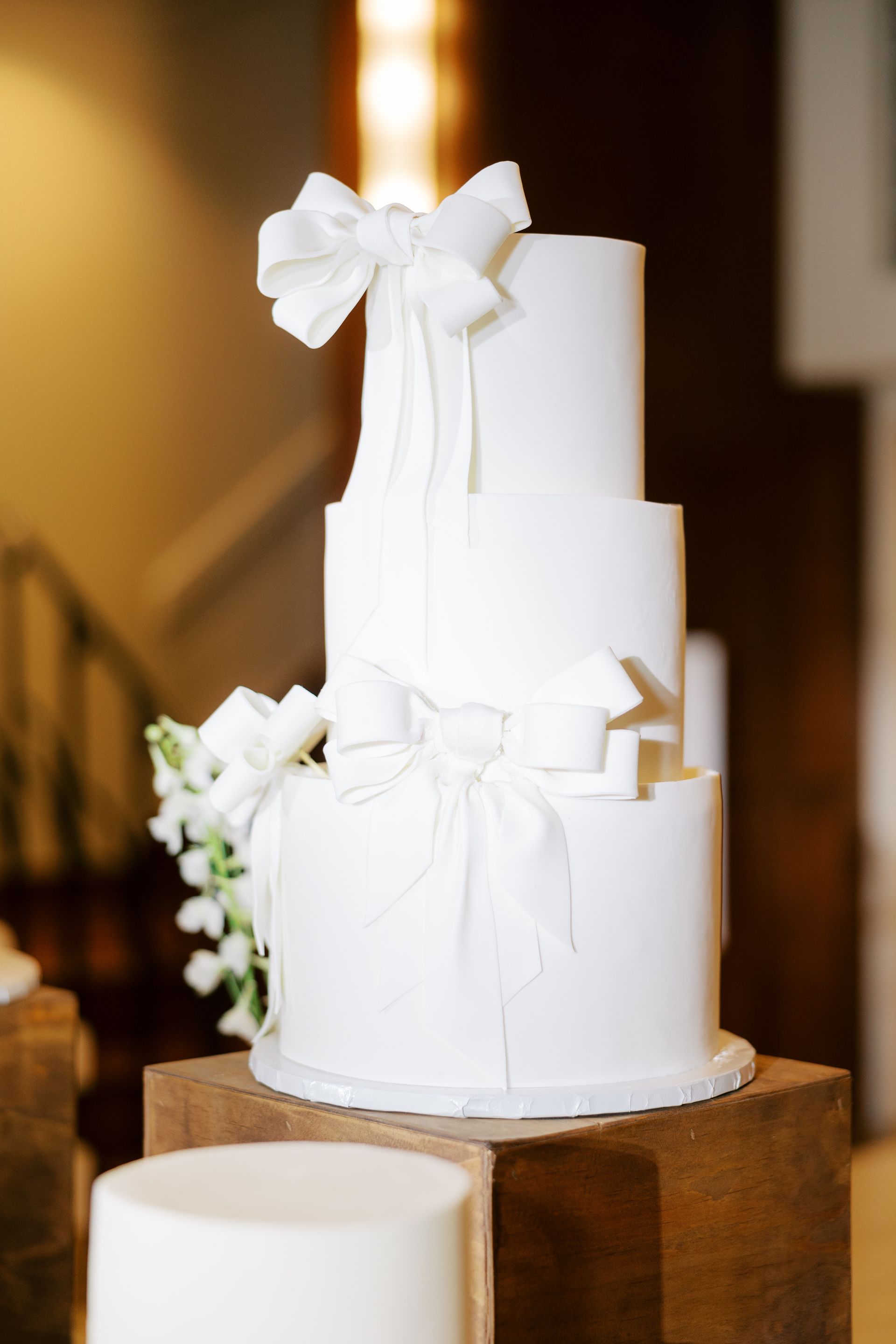 White three-tiered wedding cake with bow decorations on a wooden stand.