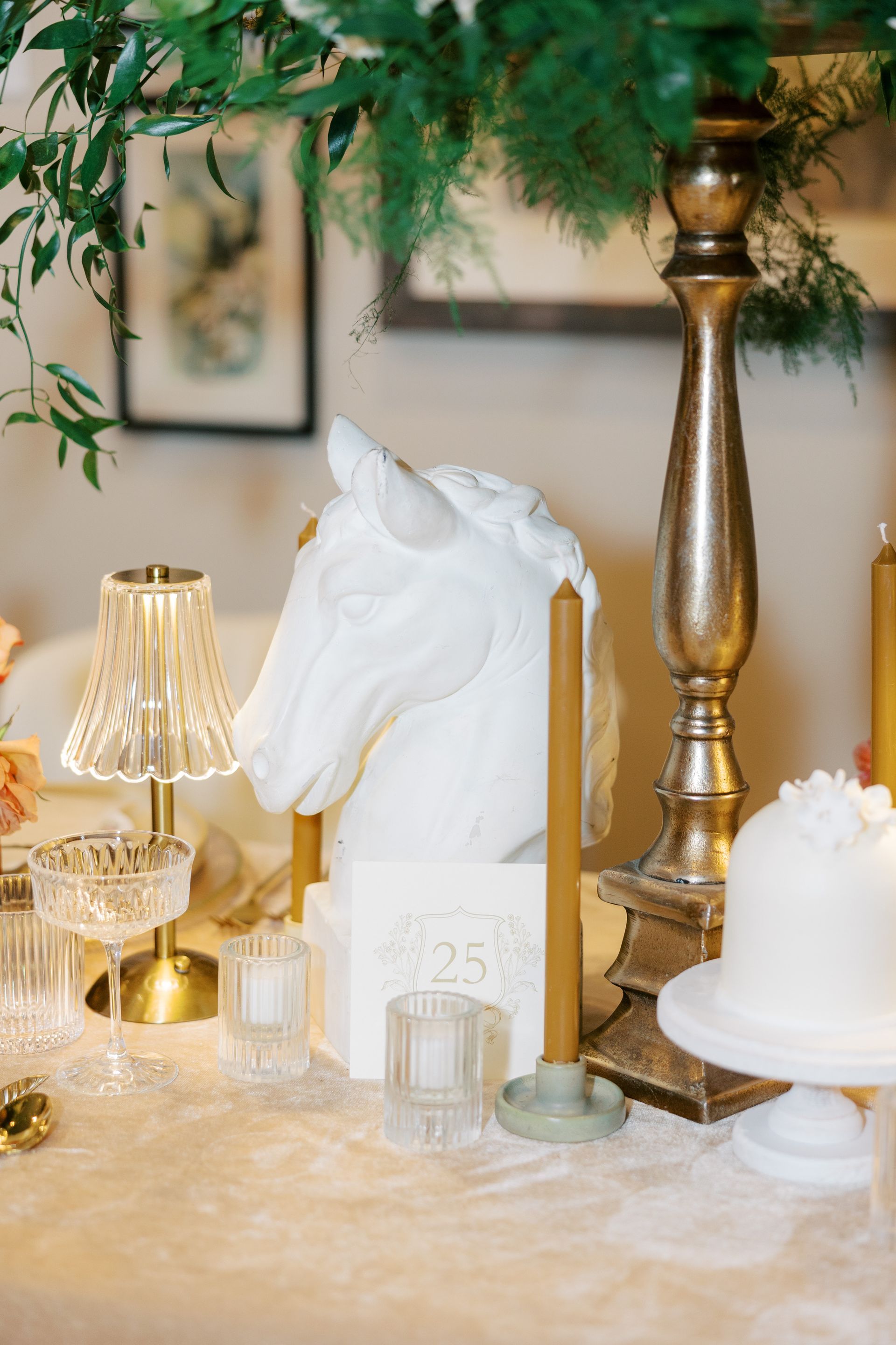 Elegant table setting with white horse bust, gold candlestick, flowers, and cake.