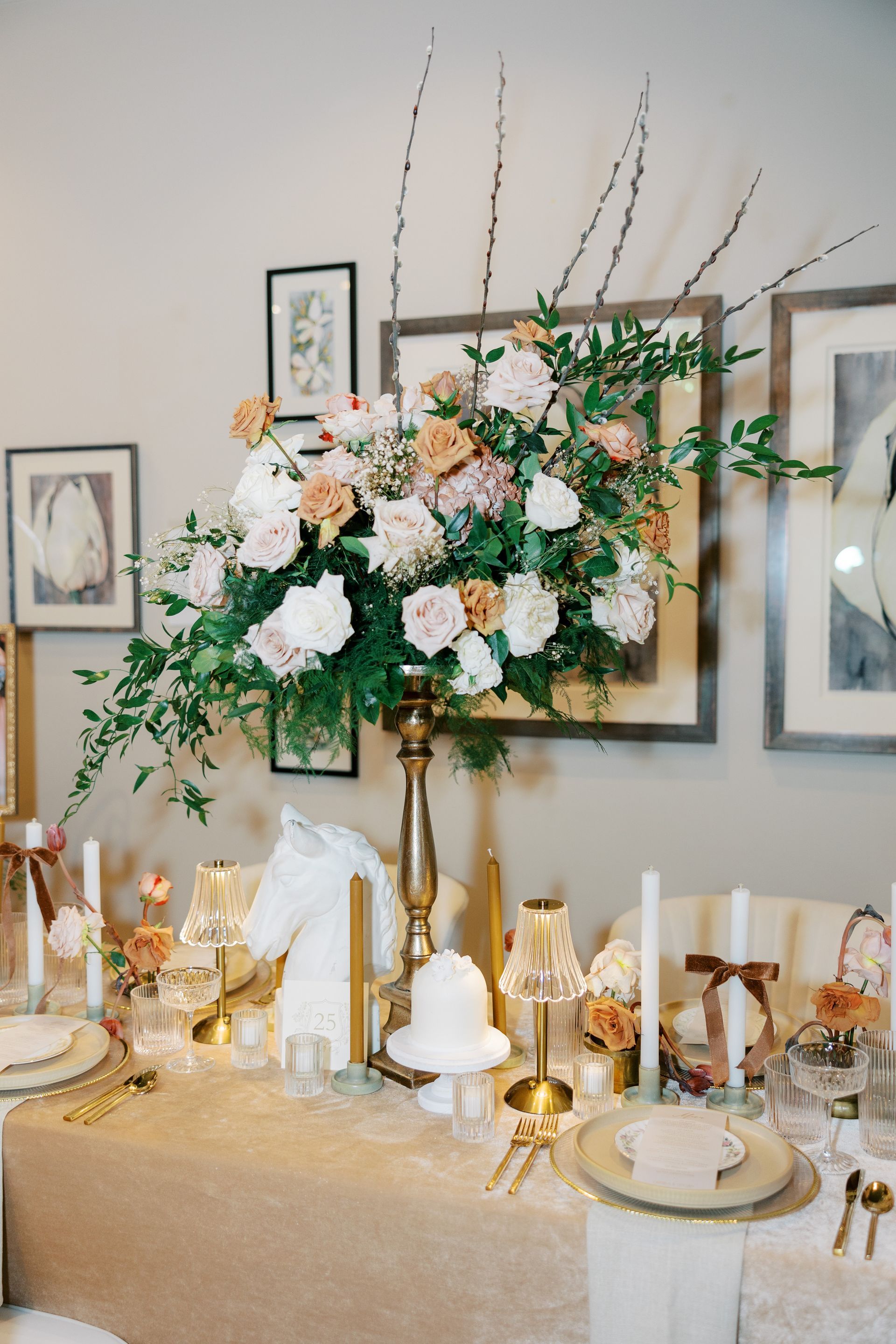Elegant table setting with large floral arrangement, candles, and framed artwork.
