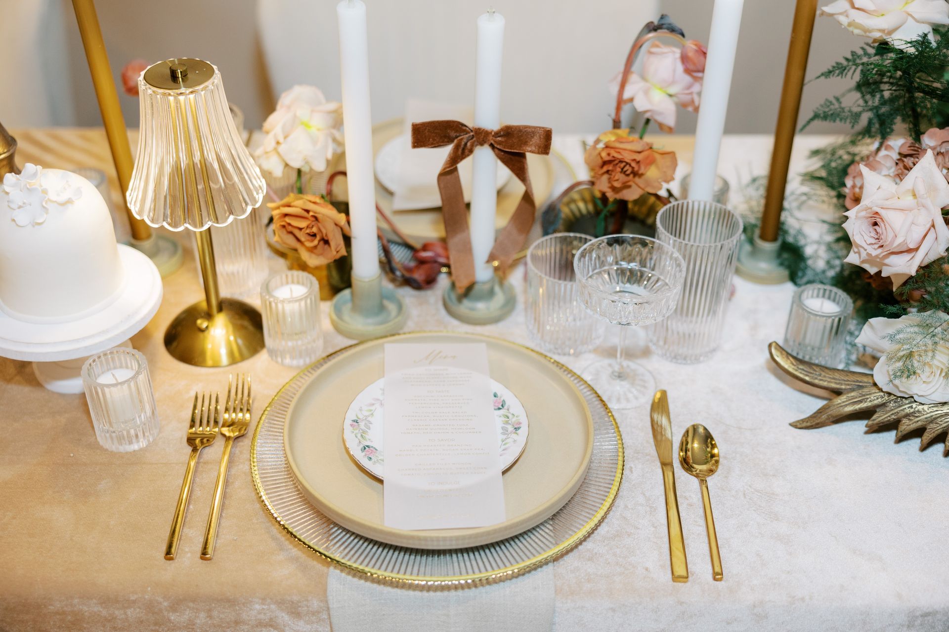 Wedding table setting with gold accents, candles, floral arrangement, and place setting with delicate details.