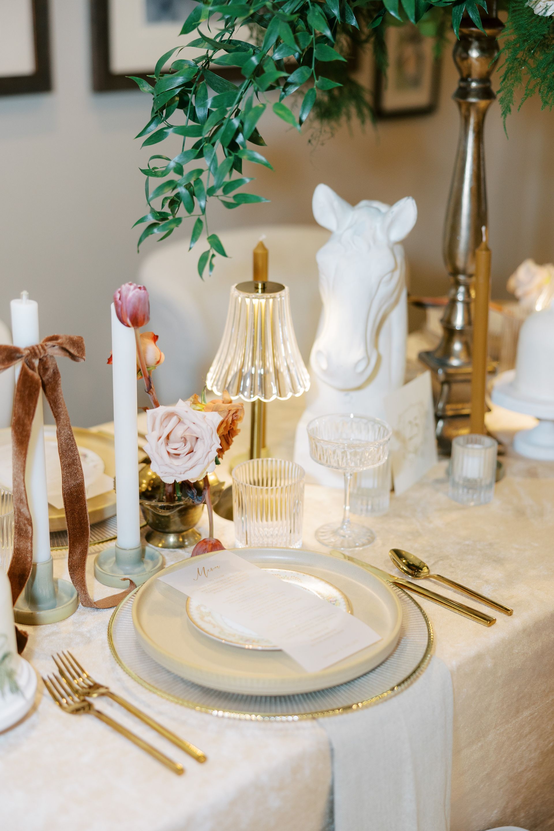 Elegant table setting with gold accents, flowers, candles, and a horse statue.