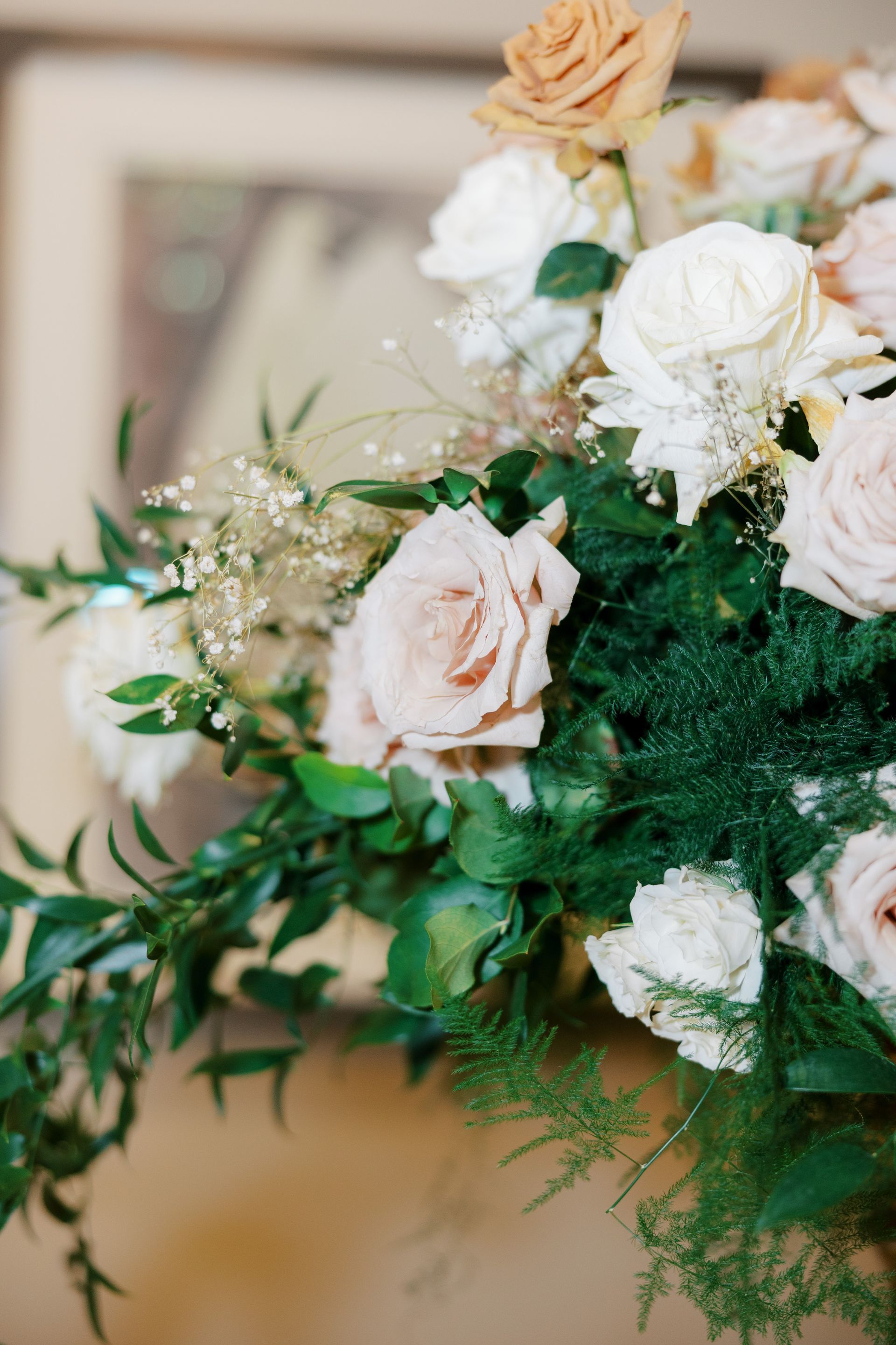 Close-up of a floral arrangement with light pink and white roses, greenery, and small white flowers.