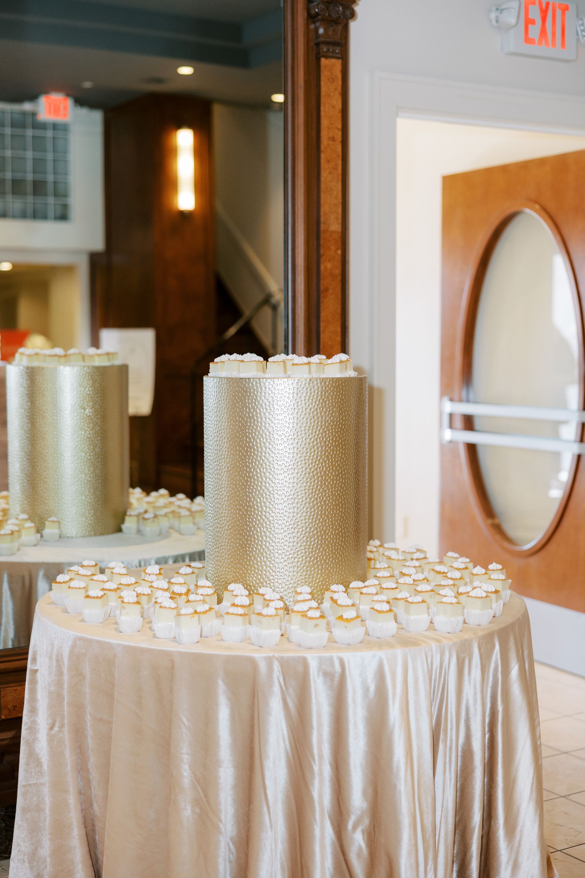 Gold sequined wedding cake and cupcakes on a round table. Mirror reflects the setup.