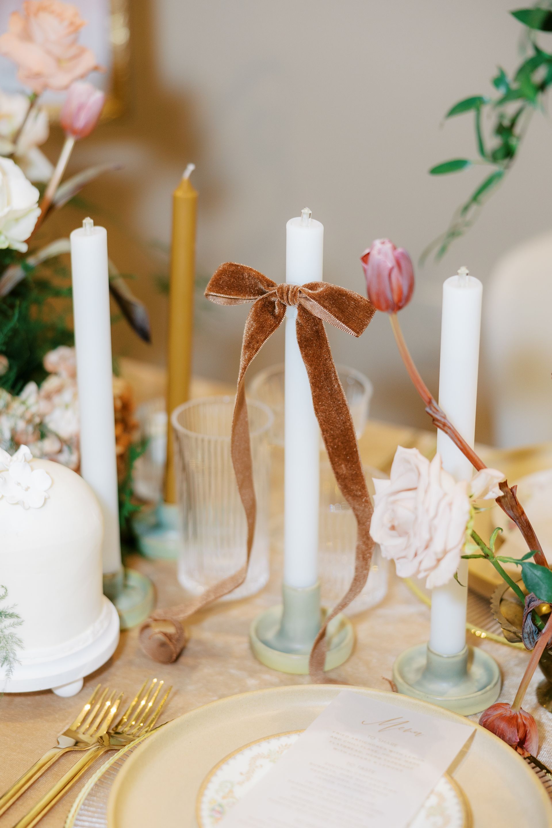Table setting with candles, flowers, and gold silverware. A brown velvet ribbon decorates the middle candle.