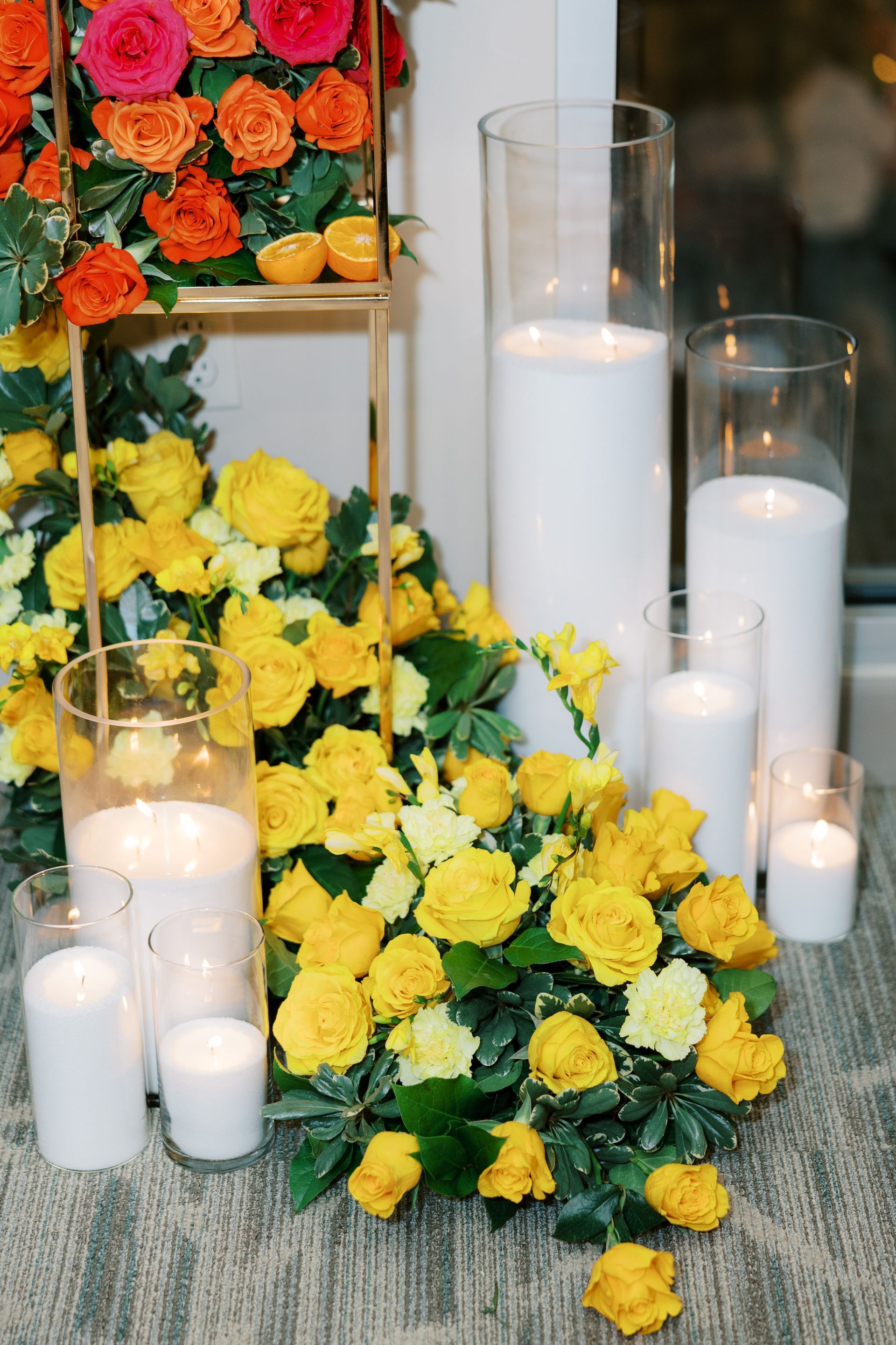 Yellow roses, orange flowers, and white candles on display.
